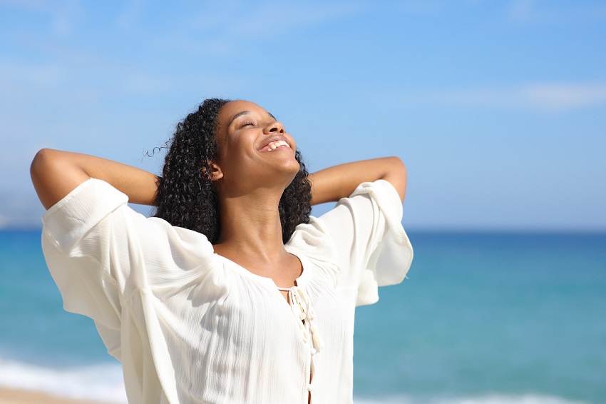 Happy black woman breathing and relaxing on the beach